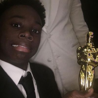 Alex R. Hibbert posing for a photo shoot while holding an award in hand.